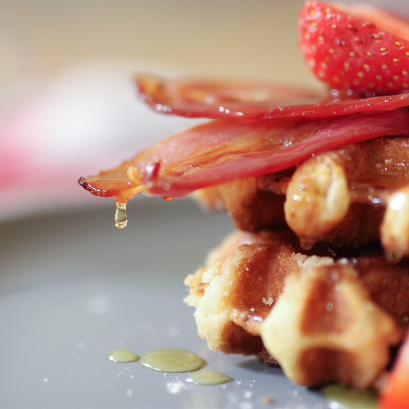 Thick waffles topped with bacon and strawberries with maple syrup dripping off