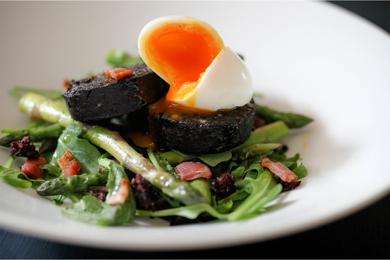 black pudding on a bed of salad and asparagus topped with a boiled egg